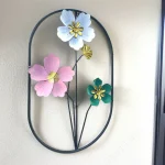 Pastel Floral Metal Wall Decor in an oval black frame with light blue, pink, and green flowers, hanging on a white wall.